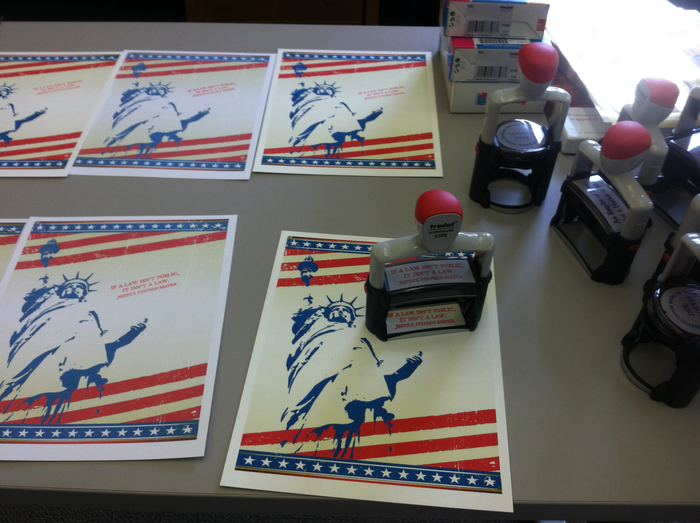 Step 1. Cover sheets are prepared with the Statue of Liberty. A Trodart self-inking red rubber stamp is used to stamp "If a law isn't public, it isn't law" on the front.